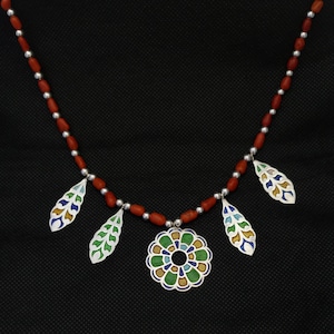 May include: A red coral bead necklace with a silver pendant featuring a colourful floral design and three leaf-shaped pendants.