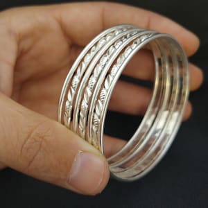 Op de afbeelding: Set van vier zilveren armbanden met ingewikkelde ontwerpen. De armbanden zijn op elkaar gestapeld en hebben een glanzende afwerking.