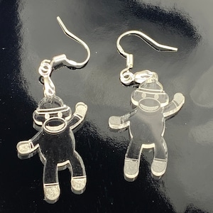 May include: A pair of clear acrylic earrings in the shape of a sock monkey. The earrings have silver-colored fish hook ear wires. The sock monkey design has a hat, arms, and legs.