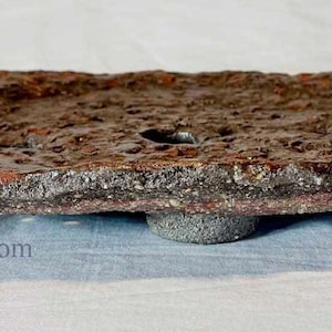 May include: A rustic, oval-shaped, brown and red decorative tray with a rough, textured surface. The tray has a small, round base and a hole in the center. The tray is made of a dark, earthy material.