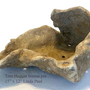 May include: A brown, rock-shaped bonsai pot with a rough, textured surface. The pot is 15 inches by 12 inches. "Tree Hugger bonsai pot 15" x 12" Linda Paul" is written below the pot.
