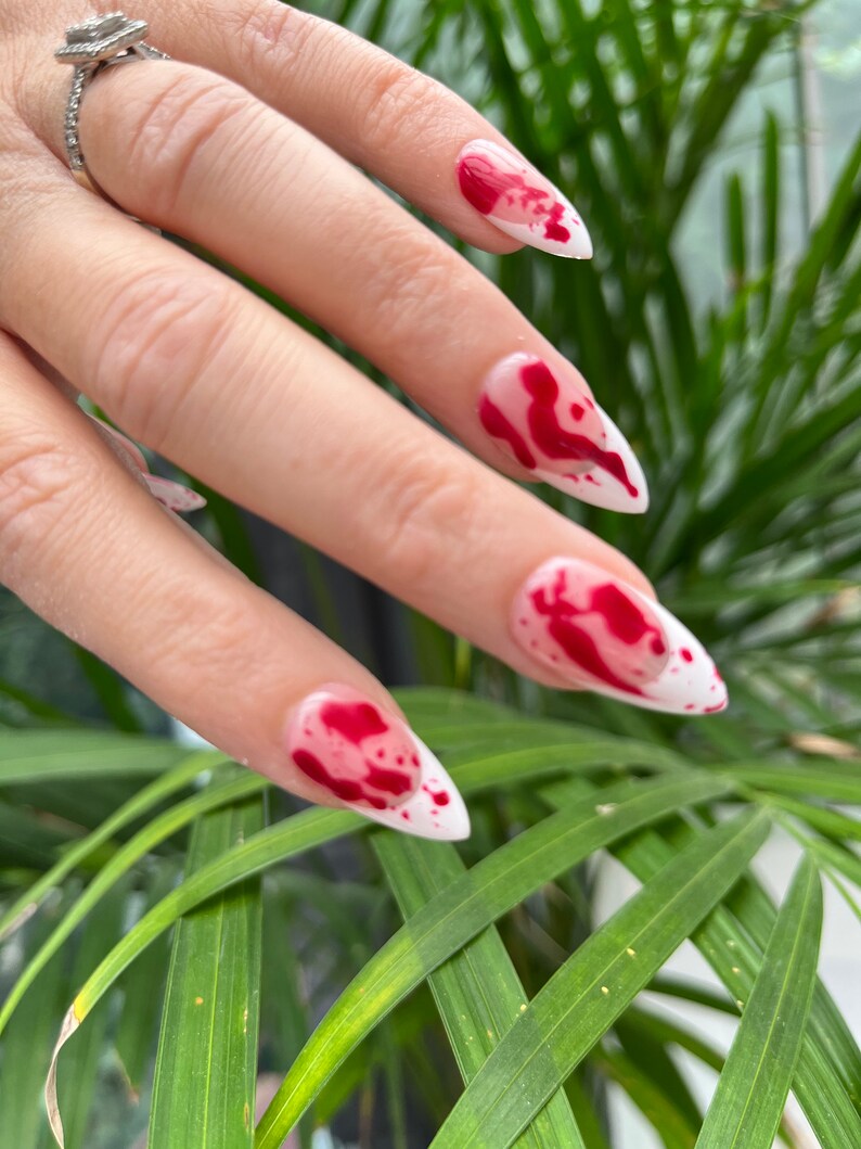 May include: White stiletto nails with red blood splatter nail art design.
