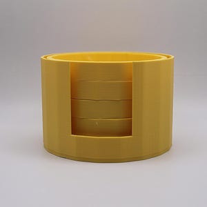 May include: A yellow plastic stackable ring holder with four rings inside. The holder is cylindrical and has a smooth surface.