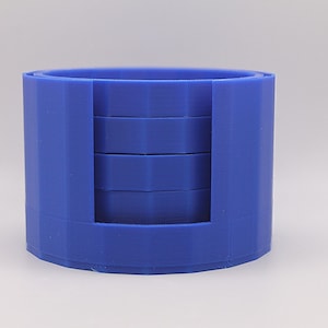 May include: A blue coaster set with a cylindrical holder. The holder has a cutout section to display the coasters. The coasters are round and fit snugly inside the holder. The set is made of a solid, durable material.