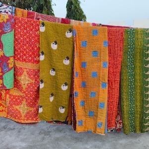 Pode incluir: Uma coleção de colchas kantha coloridas penduradas em um varal. As colchas são feitas de tecido patchwork e têm intrincados desenhos de bordado. As colchas estão em vários tons de vermelho, laranja, amarelo, verde e azul.