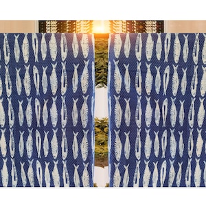 Puede incluir: Cortinas azules con un patrón repetitivo de peces blancos. La tela tiene un fondo azul oscuro con pequeños puntos blancos. Las cortinas cuelgan frente a una ventana.