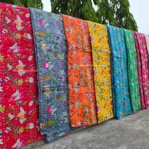Puede incluir: Una colección de colchas coloridas con estampados florales. Las colchas se exhiben en fila, mostrando una variedad de colores que incluyen rojo, azul, naranja, amarillo y rosa. Cada colcha presenta un diseño floral único y está hecha de tela acolchada suave.