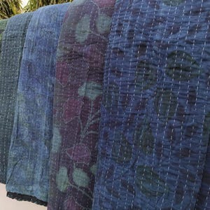 May include: Four kantha quilts in shades of blue and green with floral patterns. The quilts are folded and stacked on top of each other.