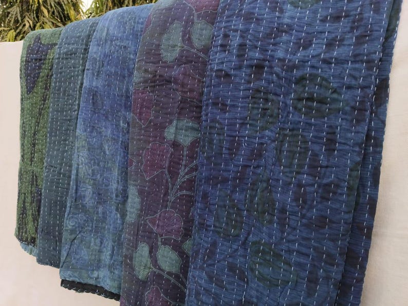 May include: Four kantha quilts in shades of blue and green with floral patterns. The quilts are folded and stacked on top of each other.