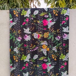 May include: Black kantha quilt featuring a floral pattern in shades of pink, green, and orange. The quilt is made of cotton and has a hand-stitched design.