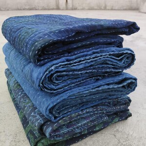 May include: A stack of four indigo blue kantha quilts, folded and layered, with intricate stitching details. The quilts are made of cotton and have a soft, textured surface.