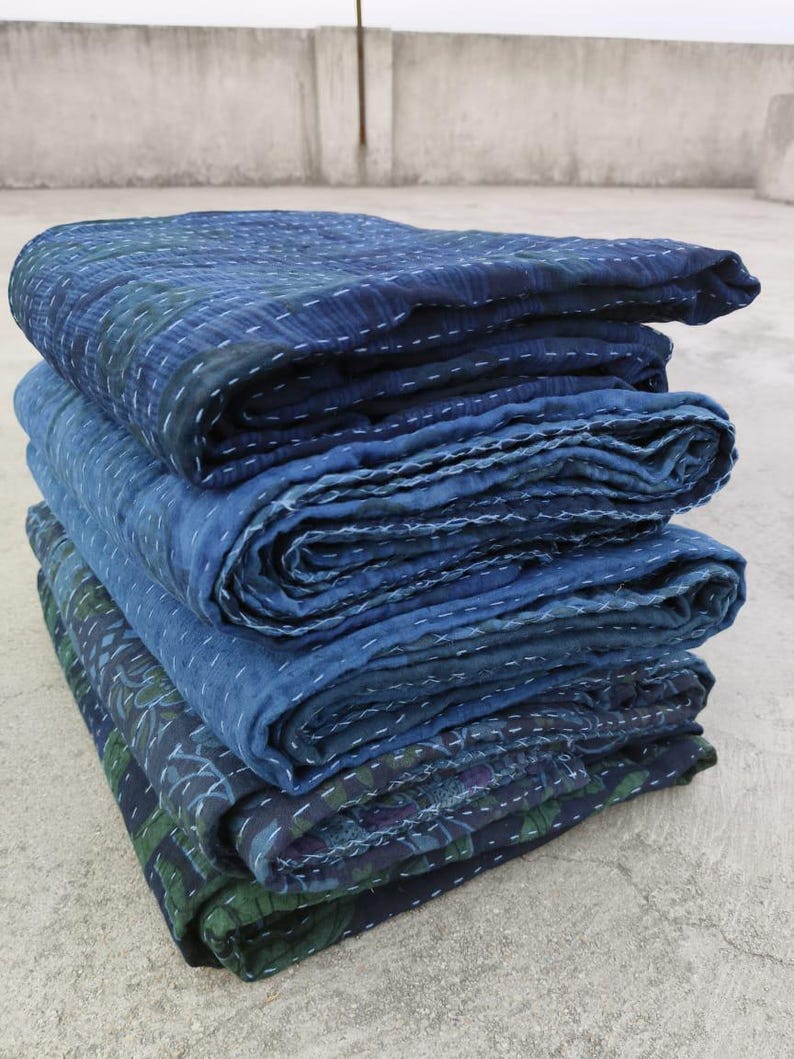 May include: A stack of four indigo blue kantha quilts, folded and layered, with intricate stitching details. The quilts are made of cotton and have a soft, textured surface.