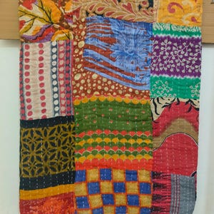 May include: A colourful patchwork quilt featuring a range of patterns and colours, including red, orange, yellow, green, blue, and purple. The quilt is made from various fabrics stitched together in a random design.