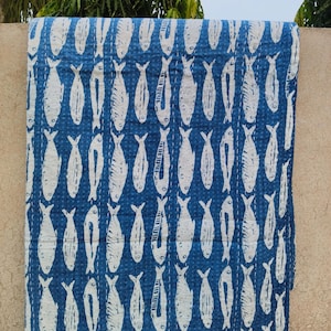 Peut inclure: Une courtepointe à motifs bleus et blancs avec un motif de poissons répété. Les poissons sont blancs sur un fond bleu foncé. La courtepointe est faite d'un tissu doux et présente des coutures visibles.