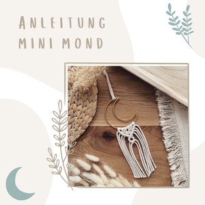 Op de afbeelding: Handgemaakte macramé wandhanger met een gouden halve maan en witte franjes. De afbeelding bevat de tekst "ANLEITUNG MINI MOND" en is geplaatst tegen een neutrale achtergrond met decoratieve elementen, wat wijst op een bohemien of minimalistische stijl.