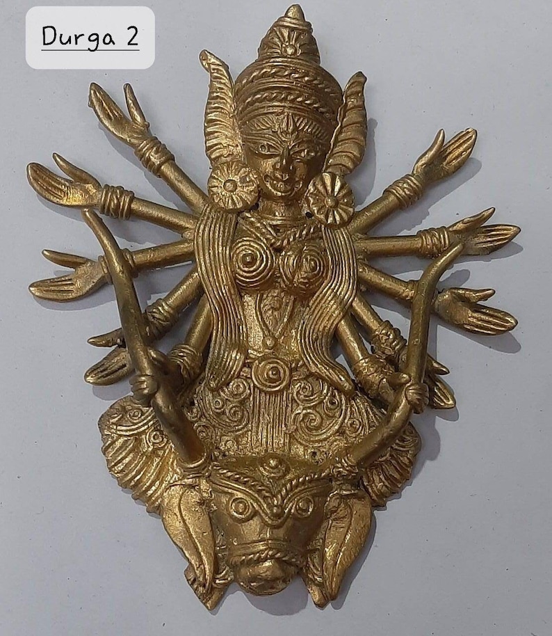 Puede incluir: Una escultura de metal dorado de la diosa hind&uacute; Durga, representada con m&uacute;ltiples brazos y montando un le&oacute;n. La escultura est&aacute; intrincadamente detallada con patrones y dise&ntilde;os ornamentados.