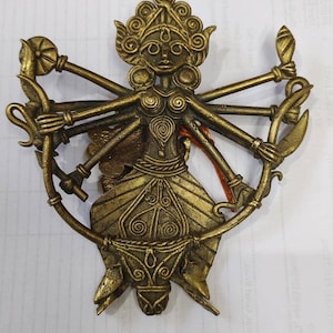 Puede incluir: Una escultura de metal dorado de la diosa hind&uacute; Durga. Se la representa con ocho brazos, cada uno sosteniendo un arma o s&iacute;mbolo diferente. La escultura est&aacute; intrincadamente detallada y tiene una forma circular.