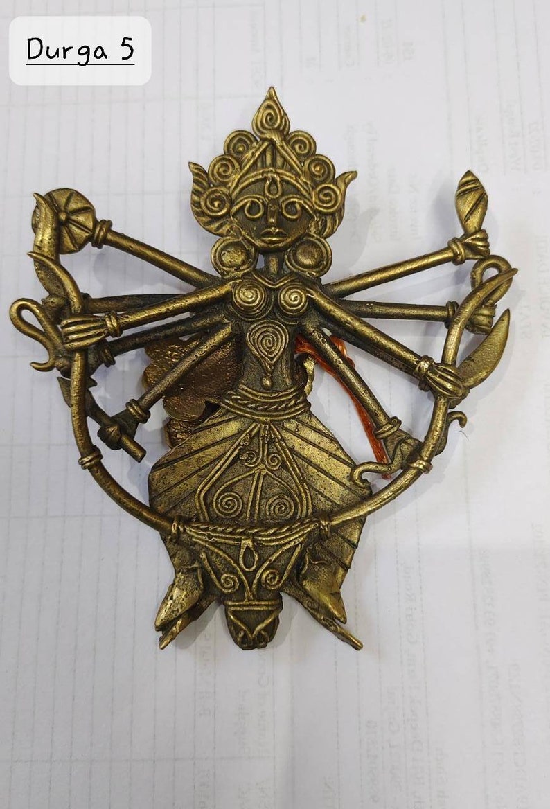 Puede incluir: Una escultura de metal dorado de la diosa hind&uacute; Durga. Se la representa con ocho brazos, cada uno sosteniendo un arma o s&iacute;mbolo diferente. La escultura est&aacute; intrincadamente detallada y tiene una forma circular.