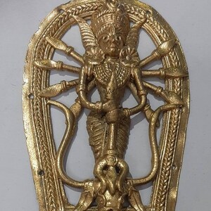Puede incluir: Un colgante de metal dorado que representa a la diosa hind&uacute; Durga. El colgante tiene forma de herradura y presenta un dise&ntilde;o detallado de Durga con m&uacute;ltiples brazos que sostienen armas. El colgante est&aacute; inscrito con el texto "Durga 3".