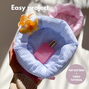 May include: A light blue gingham fabric basket holds a pink perfume bottle and is adorned with orange flowers. The text "Easy project" is at the top, and a circular graphic with "PDF PATTERN + VIDEO TUTORIAL" is on the right.