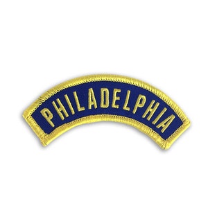 May include: A blue and gold embroidered patch with the word "PHILADELPHIA" in yellow lettering.