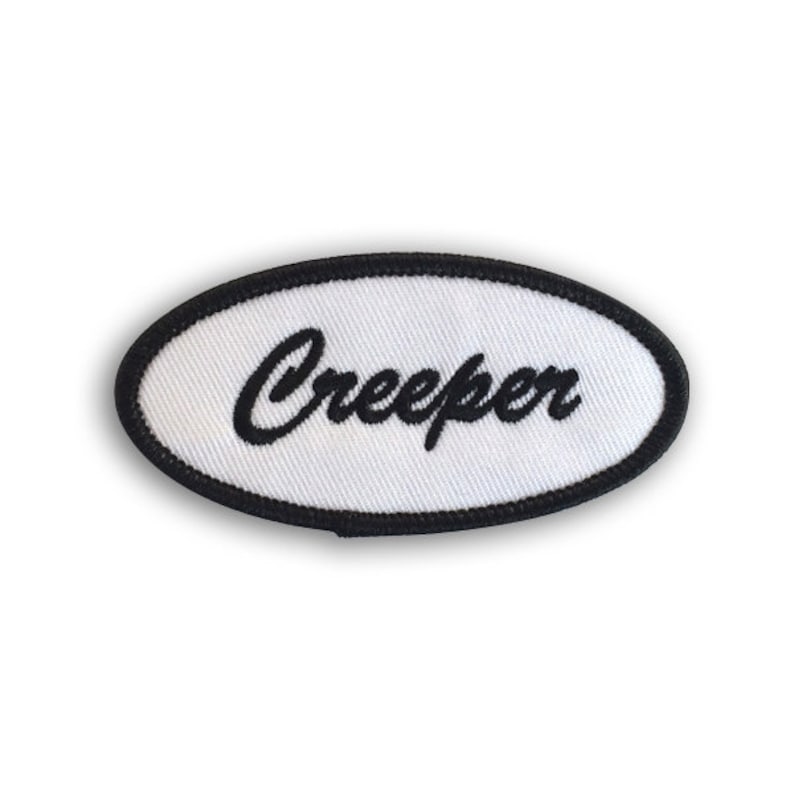May include: White oval-shaped patch with a black embroidered border and the word "Creeper" in black cursive lettering.