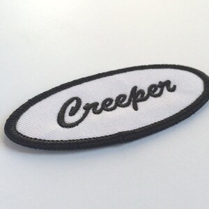 May include: White oval patch with black embroidered border and the word "Creeper" in black cursive lettering.