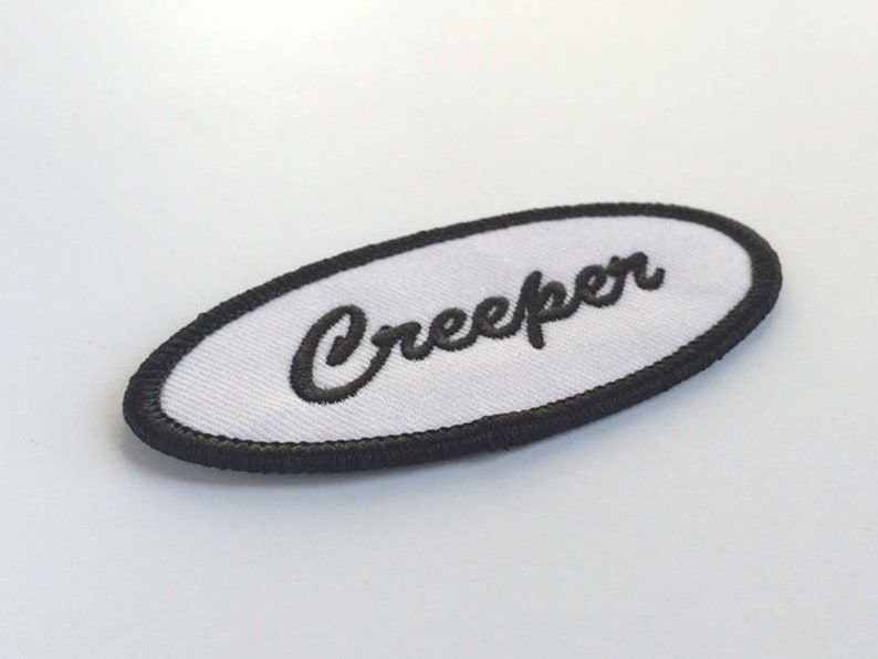 May include: White oval patch with black embroidered border and the word "Creeper" in black cursive lettering.