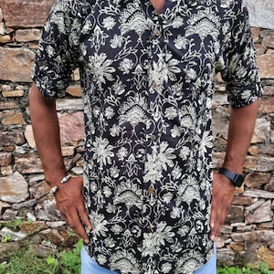 Pu&ograve; includere: Una camicia a maniche corte con bottoni, di colore nero e bianco, con un motivo floreale. La camicia ha un colletto e una chiusura con bottoni.
