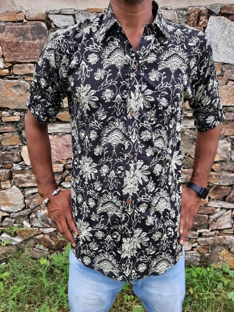 Pu&ograve; includere: Una camicia a maniche corte con bottoni, di colore nero e bianco, con un motivo floreale. La camicia ha un colletto e una chiusura con bottoni.