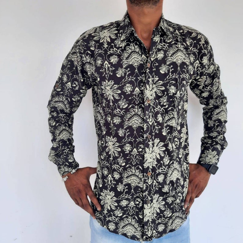 Pu&ograve; includere: Una camicia nera a maniche lunghe con un motivo floreale bianco. La camicia ha una chiusura con bottoni sul davanti e un colletto.