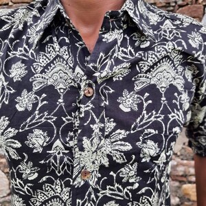 Pu&ograve; includere: Una camicia nera con bottoni e un motivo floreale bianco. La camicia ha un colletto e una chiusura con bottoni.