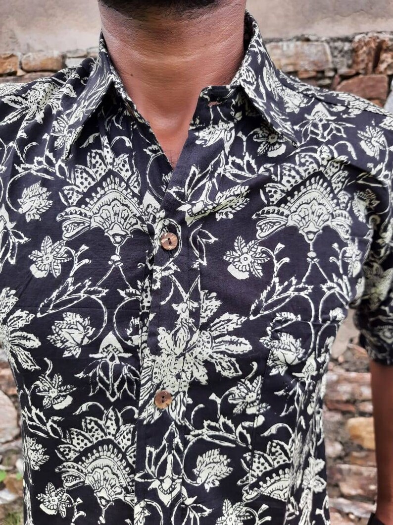 Pu&ograve; includere: Una camicia nera con bottoni e un motivo floreale bianco. La camicia ha un colletto e una chiusura con bottoni.