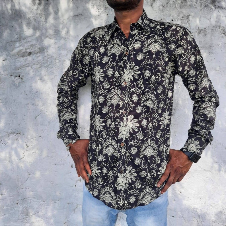 Pu&ograve; includere: Una camicia nera a maniche lunghe con un motivo floreale bianco. La camicia ha una chiusura con bottoni sul davanti e un colletto.