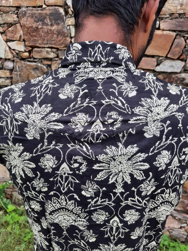 Pu&ograve; includere: Una camicia a stampa floreale bianca e nera con colletto abbottonato. La camicia presenta un design tradizionale indiano con dettagli intricati.