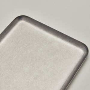 May include: A rectangular, light gray tray with rounded corners. The tray has a slightly textured surface and a darker gray border. The design is minimalist and modern, suitable for serving or display.