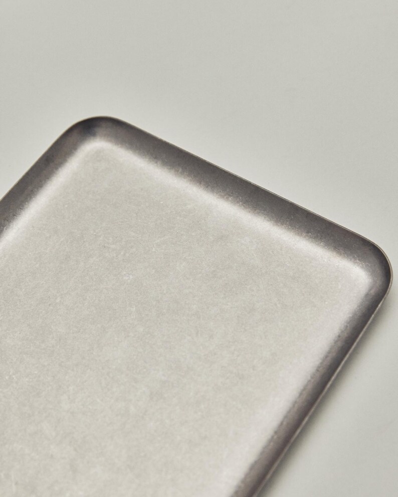 May include: A rectangular, light gray tray with rounded corners. The tray has a slightly textured surface and a darker gray border. The design is minimalist and modern, suitable for serving or display.