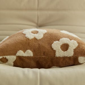 May include: A brown throw pillow with white fluffy daisy-shaped designs. The pillow is made of a soft, plush fabric.