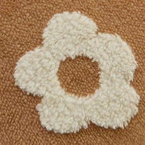 May include: A brown fuzzy fabric with a white fuzzy flower design. The flower has a circle in the center.