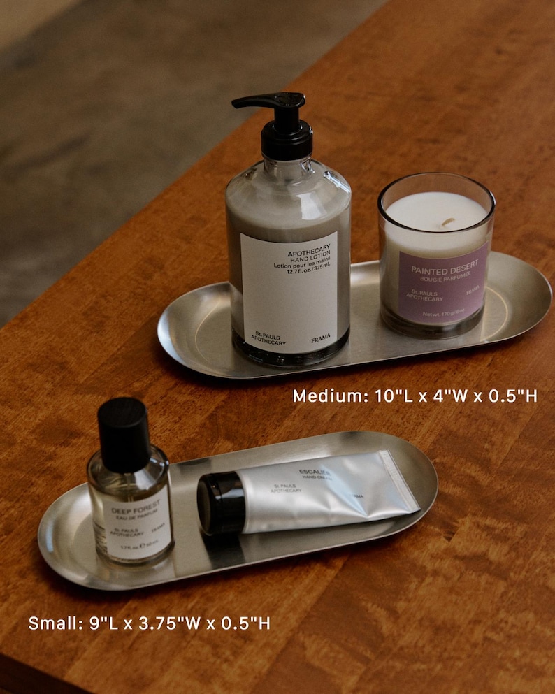 May include: Two oval stainless steel trays. The medium tray, 10"L x 4"W x 0.5"H, holds a pump bottle of hand lotion and a candle labeled Painted Desert. The small tray, 9"L x 3.75"W x 0.5"H, holds a glass bottle of perfume and a tube of hand cream.