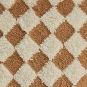 May include: A close-up of a brown and white checkered fabric with a fuzzy texture.