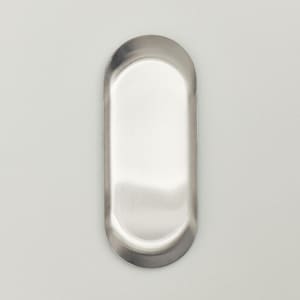May include: A small, oval-shaped metal tray with a smooth, brushed silver finish. The tray features a shallow, recessed center and a slightly raised, rounded rim that follows the elongated oval contour of the overall object design.