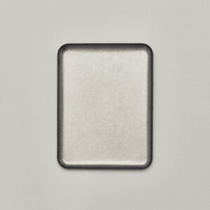 May include: A rectangular, metallic-looking tray with rounded corners. The tray has a light, brushed metal appearance with a darker border. The background is a solid, neutral color.