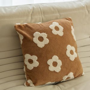 May include: A brown throw pillow with a white floral pattern. The pillow is made of a soft, plush fabric.