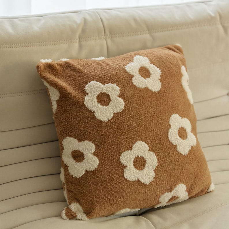 May include: A brown throw pillow with a white floral pattern. The pillow is made of a soft, plush fabric.