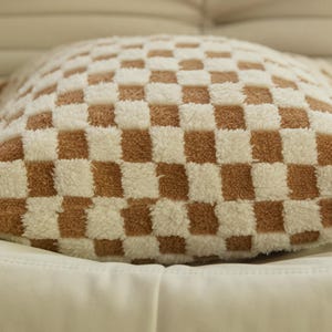 May include: A brown and white checkered throw pillow with a soft, fluffy texture.