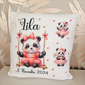 Peut inclure: Oreiller blanc avec un panda rose sur une balançoire, un panda rose tenant une fleur et un panda rose portant une robe rose. L'oreiller porte le nom "Lila" et la date "11 Novembre 2024" imprimée dessus.