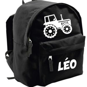 Peut inclure: Sac à dos noir avec un motif de tracteur blanc. La poche avant porte le nom "LÉO" en blanc. Il est équipé d'une poignée supérieure et de bretelles réglables. Parfait pour l'école.