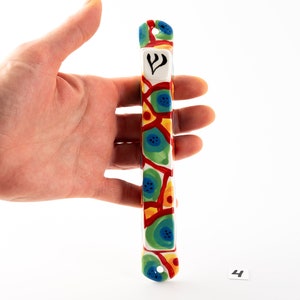 May include: A colorful ceramic mezuzah with a white background and a blue, green, red, and yellow geometric pattern. The mezuzah has a Star of David symbol on the front.