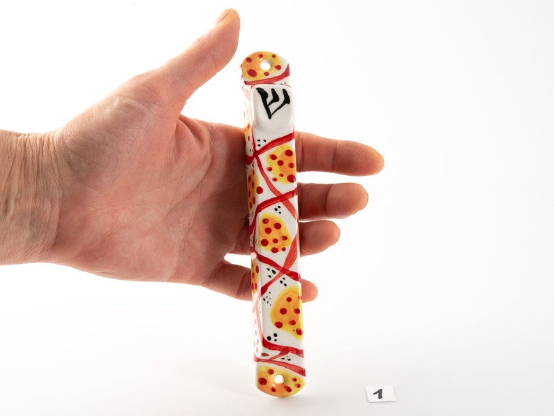 May include: A white mezuzah with a red and yellow geometric pattern. The mezuzah has the Hebrew letter "Shin" on the top.